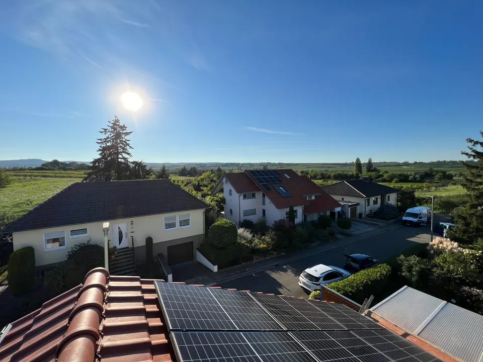 Blick vom Dach über frisch montierte Solarmodule auf Weinberge in der Pfalz